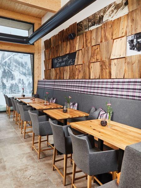 Nach „herzenslust“ genießen. Gemütliches Alpenrestaurant mit Holztischen, grauen Stühlen und Bergblick